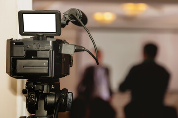 Video camera in business conference room, recording participants and speakers. Streaming video against background of event. Back view camera live path cut off. Focus on video camera display isolated