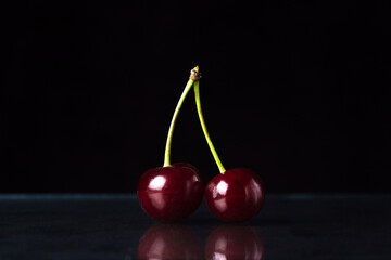 Cherry on a black background. Two red cherries on one branch
