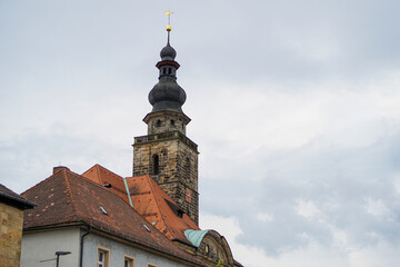 Kirchturm aus dunklem Sandstein mit roter Uhr und goldenen Zeigern, umgeben von klassischen Gebäuden. Kirche St. Georgen Bayreuth, in Bayern, Deutschland. 