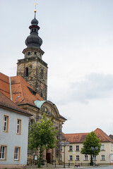 Kirchgebäude aus dunklem Sandstein mit roter Uhr und goldenen Zeigern, umgeben von klassischen Gebäuden. Kirche St. Georgen Bayreuth, in Bayern, Deutschland. 