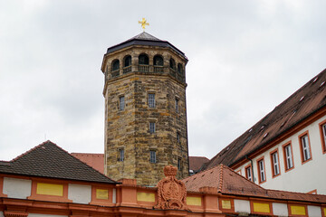 Fototapeta premium Schlossturm aus Sandstein mit Balkon und Schieferdach und goldenem Kreuz auf der Spitze. Schlossfassade im Vordergrund. Altes Schloss Bayreuth in Bayern, Deutschland.