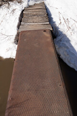 old rusty steel bridge with logs over a small river
