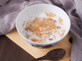 Caramelized crisps in coconut sauce (Krong-Kraeng) Sprinkled with sesame seeds in white bowl on wooden board with spoon over brown background..