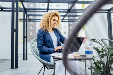 Fototapeta na wymiar Successful positive blond business woman is sitting on an outdoor terrace with a notebook in a sun lounger. Remote work with laptop in the fresh air and freelance, people lifestyle, freedom concept.
