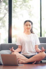 Young beautiful asian woman making mudra gesture, sitting in lotus position on the floor at home.