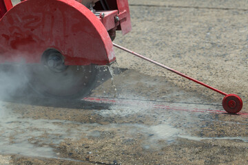 Concrete Road Cutters with worker. Worker using diamond saw blade machine cutting concrete road at...