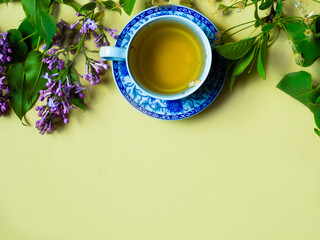 cup of green tea, apple tree flowers and lilacs on yellow background. copy space, template, horizontal