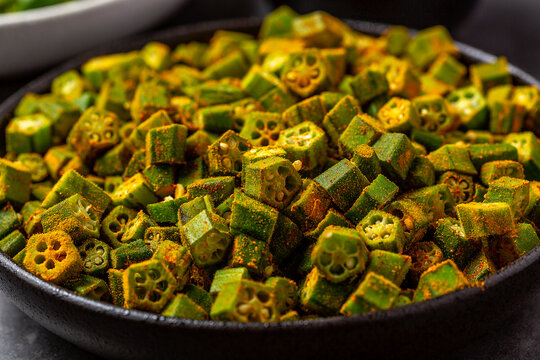 chopped raw okra mixed with turmeric powder in a bowl, preparation for indian vegetable bhindi fry