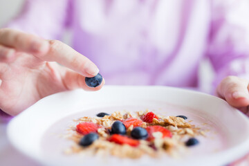 Woman putting blueberry in granola meal, diet breakfast concept.
