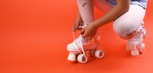 Little child with roller skates, a blue helmet on a red background, tying shoelaces. A girl of 7...