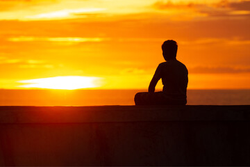 a man sitting on the shore of the ocean at sunset and meditating