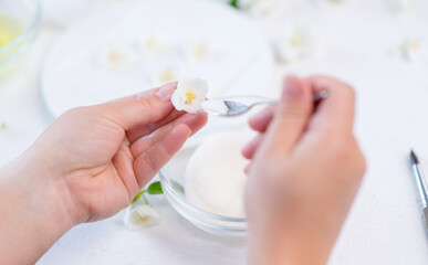 The cook’s hands hold a jasmine flower in their hands and use a spoon to pour sugar on the iced flower. Decor for cake concept.