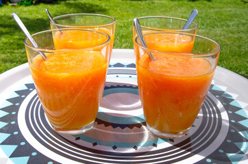 Glasses of orange juice with rapped carrots, grass background