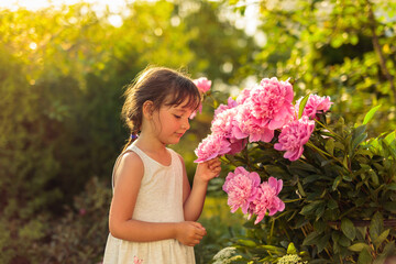 Fototapeta premium Little girl in the garden with pink peonies.