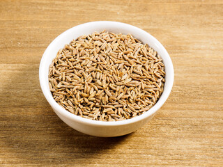 Spice cumin (jeera) in white bowl on brown wood background