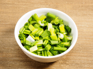 Chopped green onion in white bowl on brown wood background