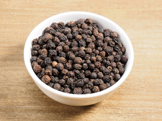 Spice black pepper in white bowl on brown wood background