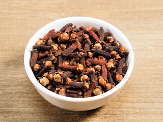 Spice cloves in white bowl on brown wood background. Healthy eating, ayurveda, naturopathy concept