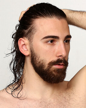 Attractive male model with long hair and beard posing in studio on isolated background. Style, trends, fashion concept.
