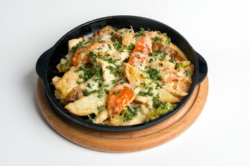 Dish on a black pan, which stands on a wooden stand. Potatoes with cheese and red pepper. Sprinkled with green parsley.