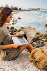 Young pretty female freelancer working on a laptop while traveling by the sea, remote work concept