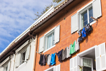 Colorful drying clothes against house facade. Traditional building exterior with window shutters, clothesline and grass on the roof in Spain. Spanish architecture. Clean dry clothes on rope.