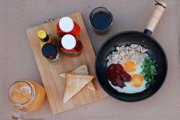 pan fried egg with toppings, Chinese sausage and pork sausage in the black pan with flavoring, slice of bread and water.
