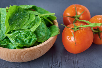 Fresh spinach leaves in wooden bowl and tomato on dark background. Organic food