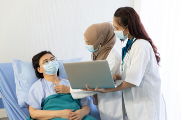 Young Asian woman Muslim doctor and assistance check up to elderly patient sitting in bed at...