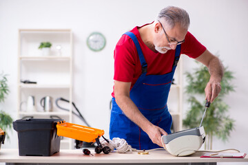 Old male contractor repairing air-conditioner indoors