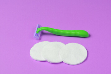 Beauty still life, minimalism. Plastic epilator razor with cotton circles on purple background. Women's accessories for beauty care.