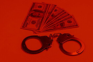 Steel handcuffs and one hundred dollar bills on in red light. Crime, corruption concept