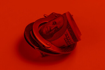 Steel handcuffs and one hundred dollar bills on in red light. Crime, corruption concept