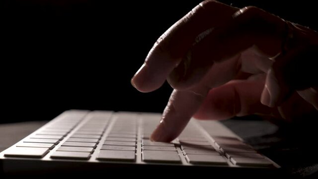 Close-up of female hands typing, typing on computer white keyboard on black background. Footage is shot in real time with artificial professional lighting in FullHD