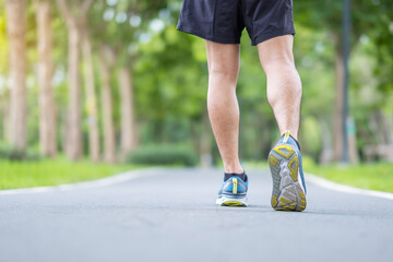 Young adult male in sport shoes running in the park outdoor, runner man jogging and walking on the road at morning, leg muscles of Athlete. Exercise, wellness, healthy lifestyle and workout concepts