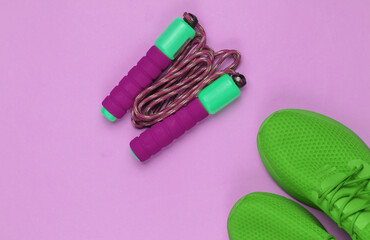 Minimalistic sport still life. Sports outfit. Sports shoes for training and jump rope on purple background. Top view