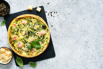 Pie (quiche) with salmon, spinach and cheese on a stone board on a concrete background. View from above.