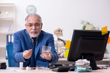 Old male sick employee working overtime in the office