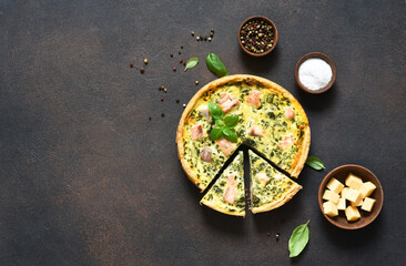 Quiche (pie) with salmon, spinach and soft cheese on a dark concrete background. View from above.