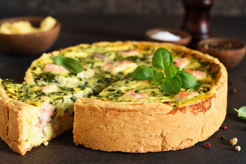 Quiche (pie) with salmon, spinach and soft cheese on a dark concrete background. Slice quiche.