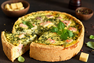 Quiche (pie) with salmon, spinach and soft cheese on a dark concrete background. Slice quiche.