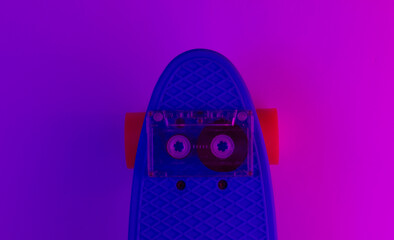 Retro 80s objects. Plastic mini cruiser board and audio tape on background with blue pink neon...