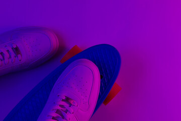 White sneakers on plastic mini cruiser board with purple pink neon gradient ligh. Top view