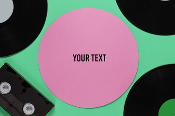 Retro vinyl records, video cassette on green background with pink circle for copy space. Top view
