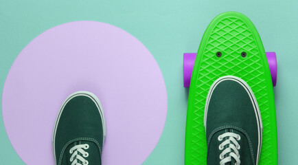 Cruiser board and sneakers on green background with a pink pastel circle. Youth hipster concept. Summer fun. Top view