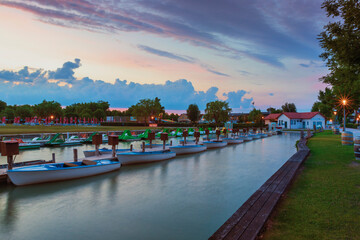 View of the mooring of small boats in the town of Podersdorf on Lake Neusiedl in Austria. In the background is a dramatic sunset sky.