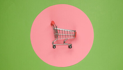 Shopping cart on green background with  pink pastel circle. Minimalistic shopping concept,...