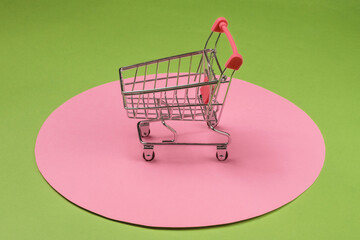 Shopping cart on green background with  pink pastel circle. Minimalistic shopping concept, shopaholic.