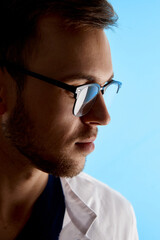 Closeup profile portrait of doctor in white medical coat and glasses with a serious face expression isolated on blue wall background