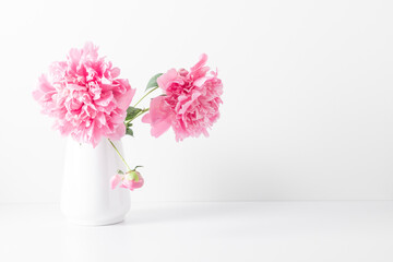 Minimal floral composition of pions on white shelf. Beautiful flowers pink peonies in vase on white background.